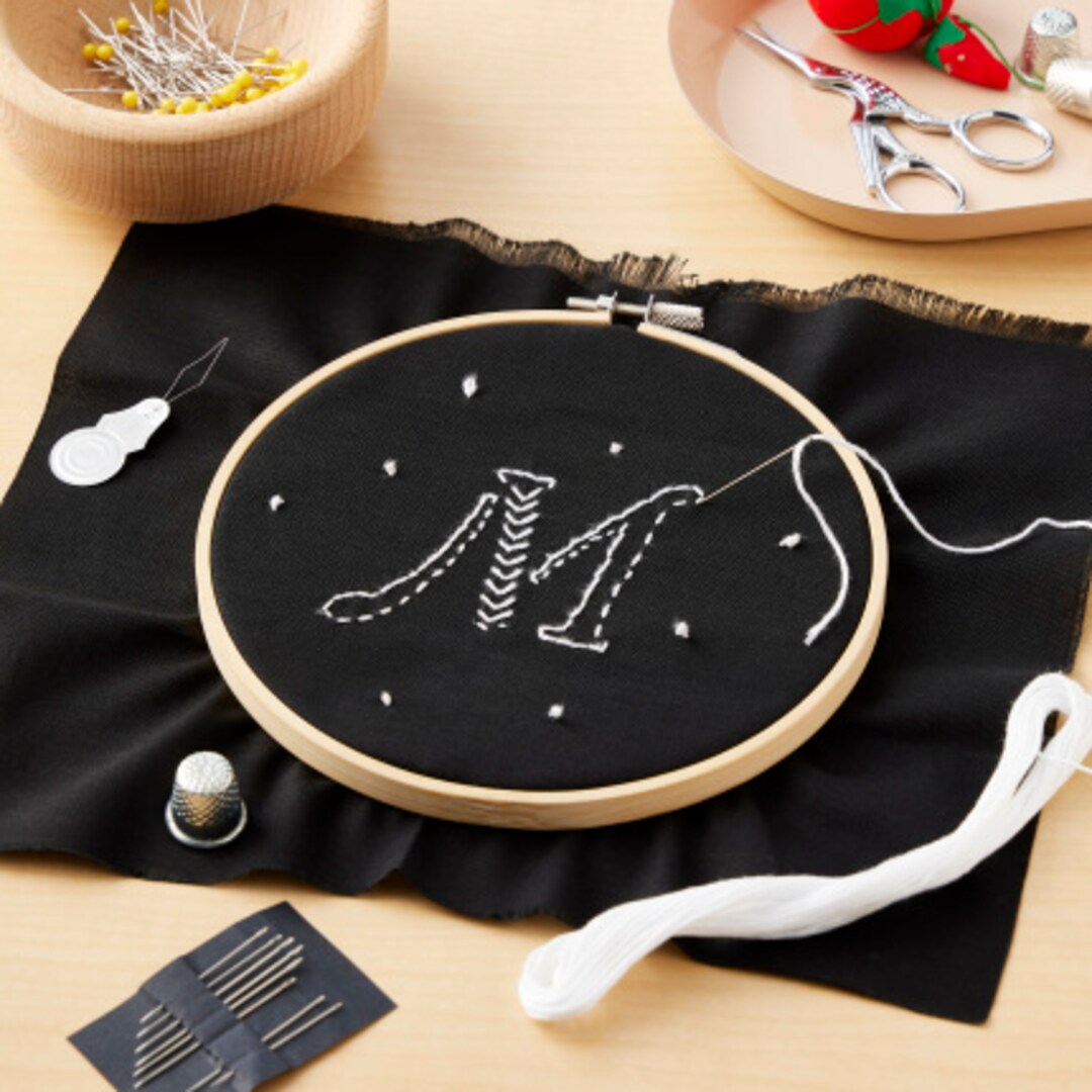 embroidery hoop with black fabric and white thread M initial pattern